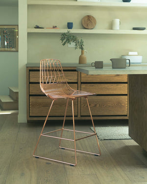 The signature Lucy Stool in Orange nestled up to a kitchen counter. The Lucy Stools are a wire design made for both outdoor and indoor dining.